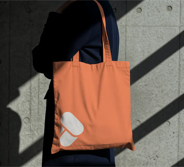 An orange Bayeux tote bag carried against a concrete wall