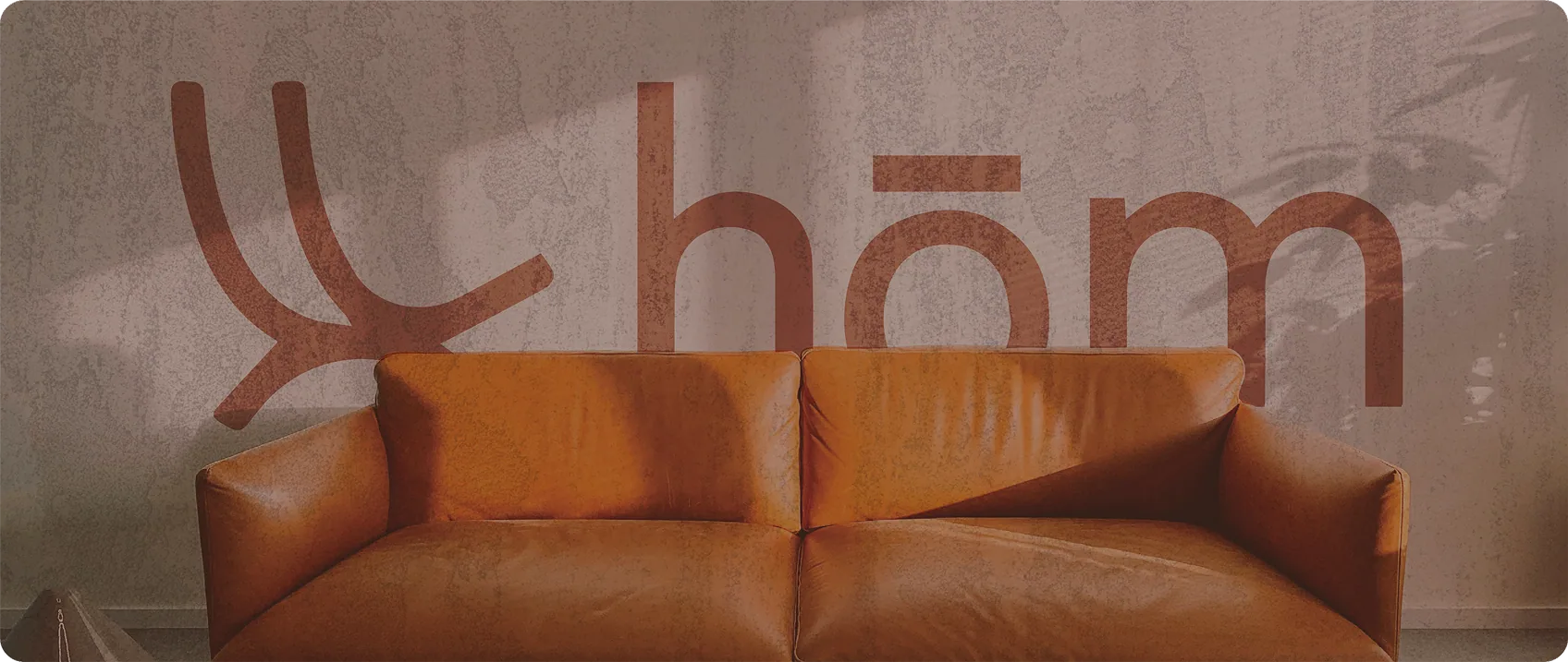 The hōm mark painted large on a plaster wall behind a tan leather sofa